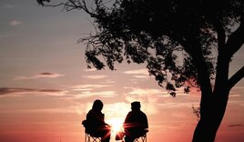 Zwei Menschen sitzen auf Stühlen, im Hintergrund der Himmel - Copyright: harlimarten / unsplash.com