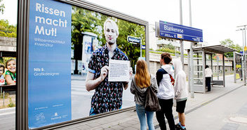 Drei Jugendliche schauen ein Plakat zu 'Rissen macht Mut' an - Copyright: Tobias Stäbler