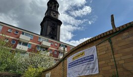 Ein Banner hängt an der Mauer einer Kita. Im Hintergrund ist der Turm der St. Michaelis Kirche in Hamburg zu sehen - Copyright: Christian Schierwagen