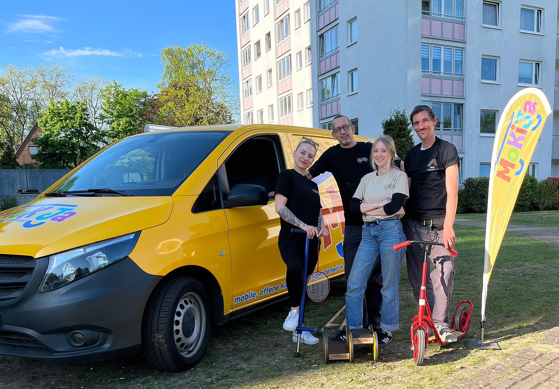 Die Mitarbeitenden von Mokija stehen vor dem gelben Auto