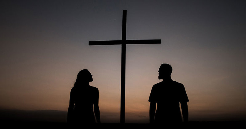 Zwei Menschen im Sonnenuntergang vor einem Kreuz