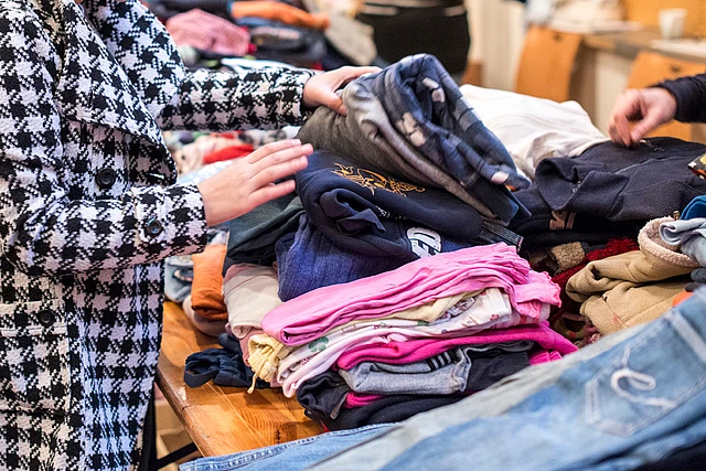 Frau sucht Kleidungsstücke bei einer Kleiderausgabe durch.