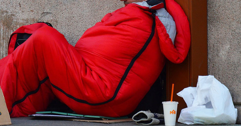 Obdachloser sitzt im winter auf der Straße, in einem dicken Schlafsack