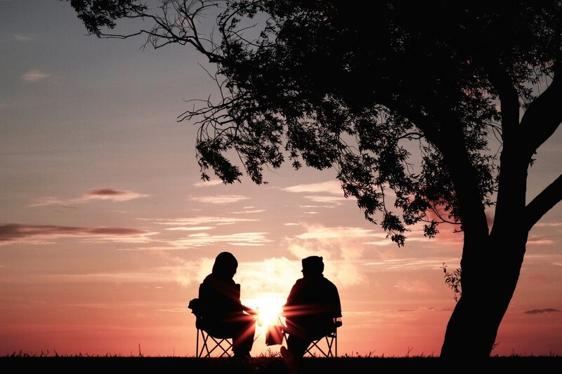 Zwei Menschen sitzen auf Stühlen, im Hintergrund der Himmel