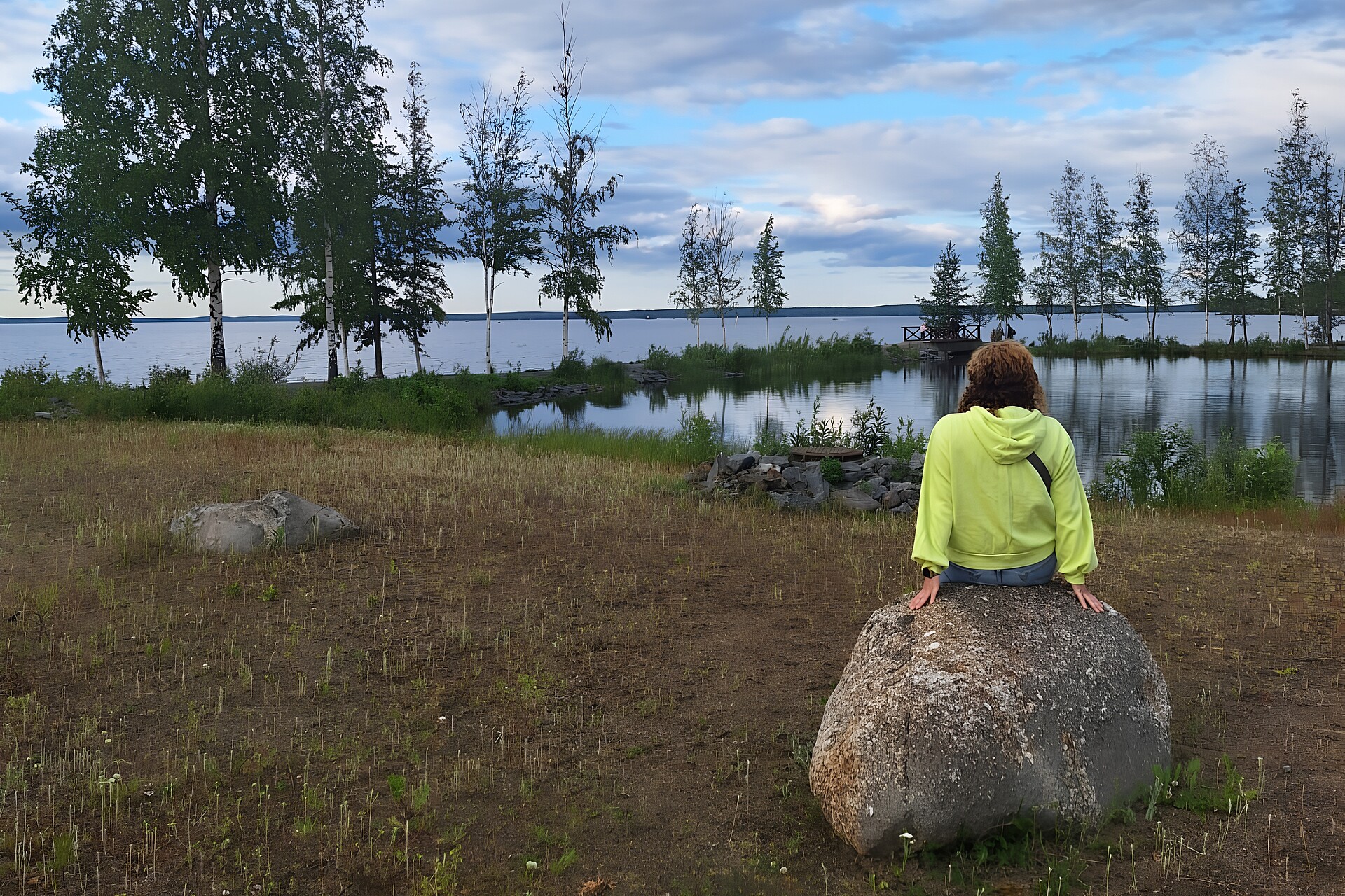 Eine Frau sitzt in Finnland auf einem Felsen, vor ihr en See