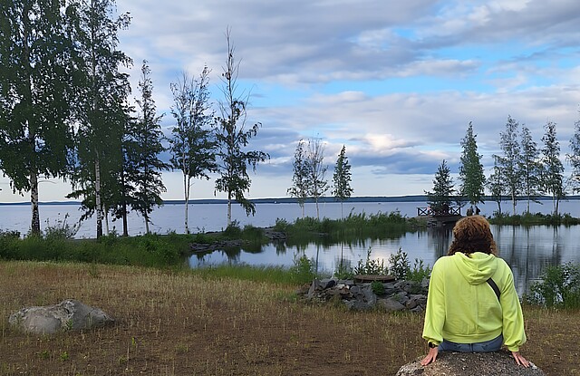Eine Frau sitzt in Finnland auf einem Felsen, vor ihr en See