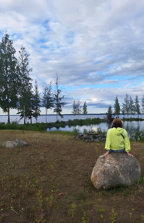 Eine Frau sitzt in Finnland auf einem Felsen, vor ihr en See