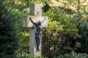 Ein steinernes Kreuz mit Jesus steht auf einem evangelischen Friedhof