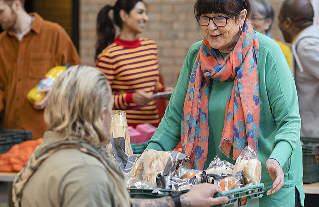 Eine Frau gibt Lebensmittel aus an einen Menschen im Rollstuhl.