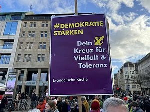 Auf einer Demonstration in Hamburg wird ein Schild hochgehalten mit der Aufschrift "Demokratie stärken, dein Kreuz für Vielfalt und Toleranz"
