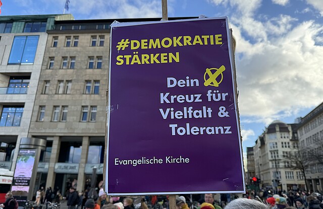 Auf einer Demonstration in Hamburg wird ein Schild hochgehalten mit der Aufschrift "Demokratie stärken, dein Kreuz für Vielfalt und Toleranz"