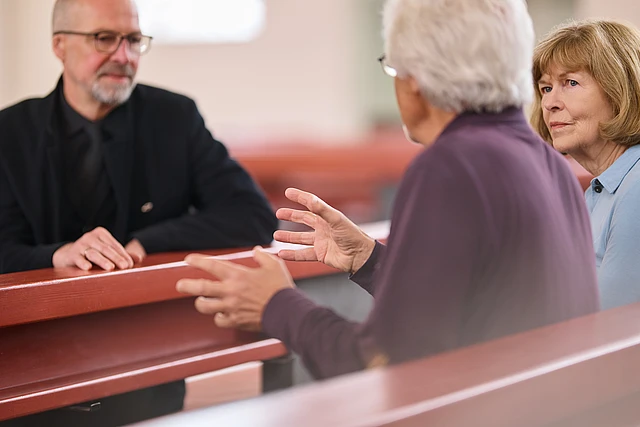 Ein Pastor im Seelsorge-Gespräch mit einem älterem Ehepaar in der Kirche.