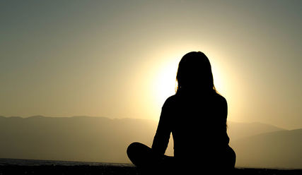 Eine Frau meditiert bei Sonnenaufgang. - Copyright: Dingzeyu Li/Unsplash