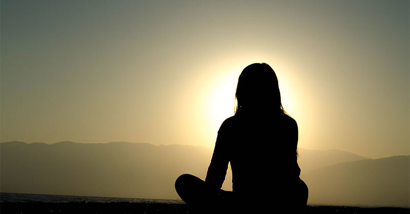 Eine Frau meditiert bei Sonnenaufgang.
