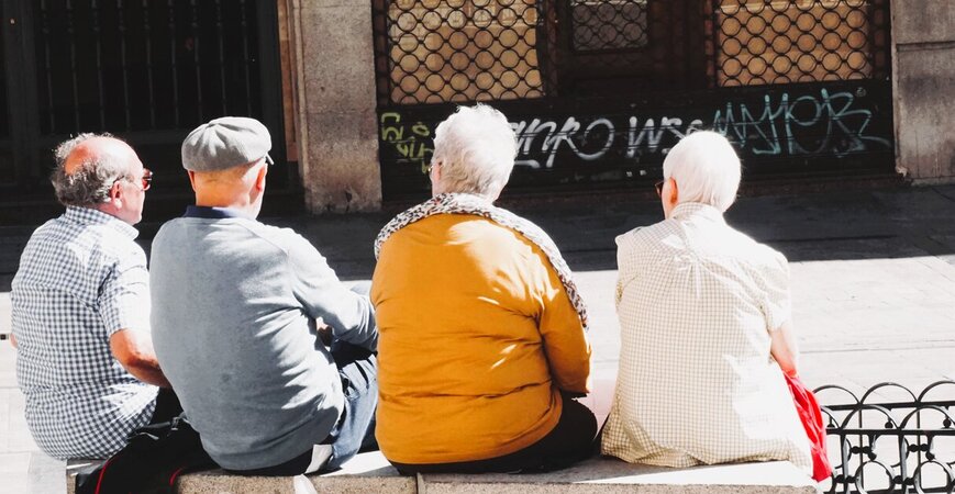 Vier Senioren die auf Steinpollern auf dem Marktplatz sitzen und sich unterhalten - Copyright: Beth Macdonald