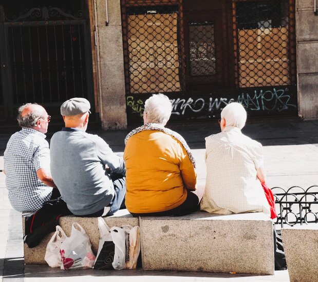 Vier Senioren die auf Steinpollern auf dem Marktplatz sitzen und sich unterhalten