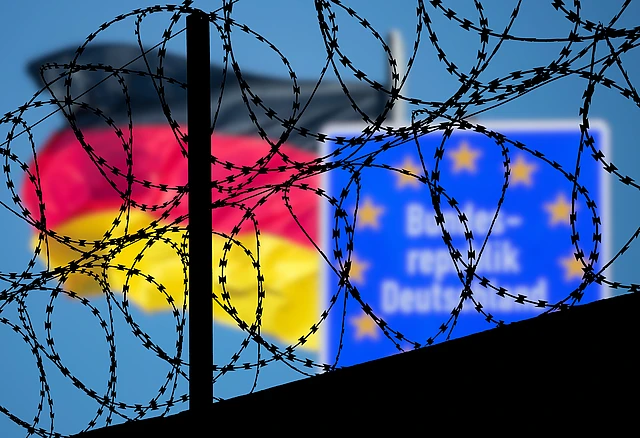 Eine Deutschlandfahne und ein Schild Bundesrepublik Deutschland hinter einem Stacheldraht-Grenzzaun.