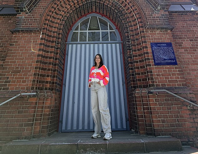 Eine Frau, Rebecca Assif, steht vor einem Kirchturm