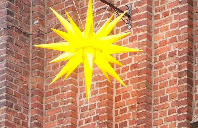 Herrnhuther Weihnachtsstern vor roter Backsteinkirche.