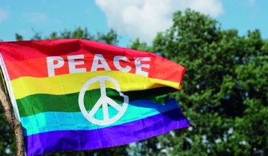 Rot-gelb-grün-hellblau-blau gestreifte wehendeFlagge mit Aufschrift PEACE und Friedenssymbol. - Copyright: Pixabay