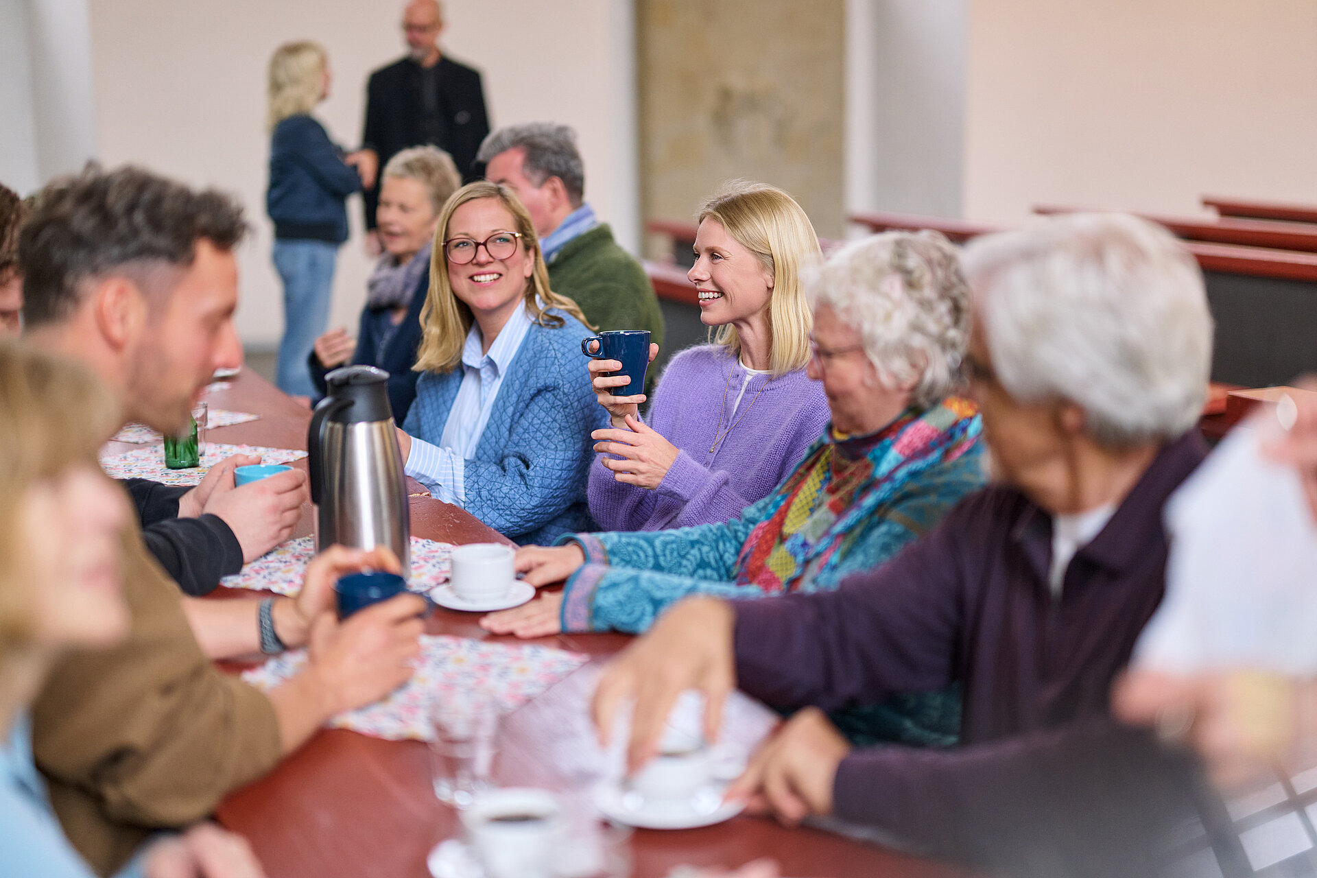Menschen sitzen an einem langen Tisch in der Kirche und unterhalten sich.