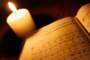 Ein Gesangbuch mit dem Choral "Verleih uns Frieden gnädiglich" wird vom Licht einer Kerze angestrahlt.