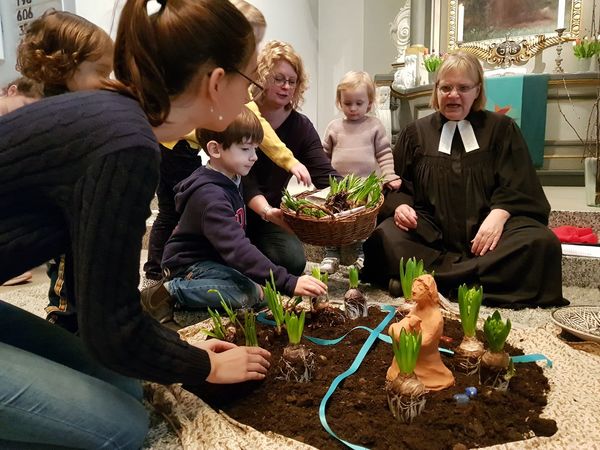 Pastorin mit Kindern auf dem Boden vor dem Altar. Es werden Blumenzwiebeln gepflanzt. - Copyright: Katja Richter