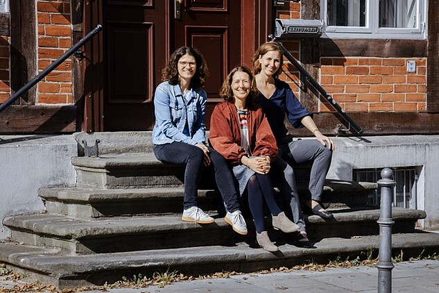 Myriel Burkhardt, Maren Gutmann und Sonja Krajewski sitzen auf steinernen Eingangsstufen und lächeln in die Kamera.