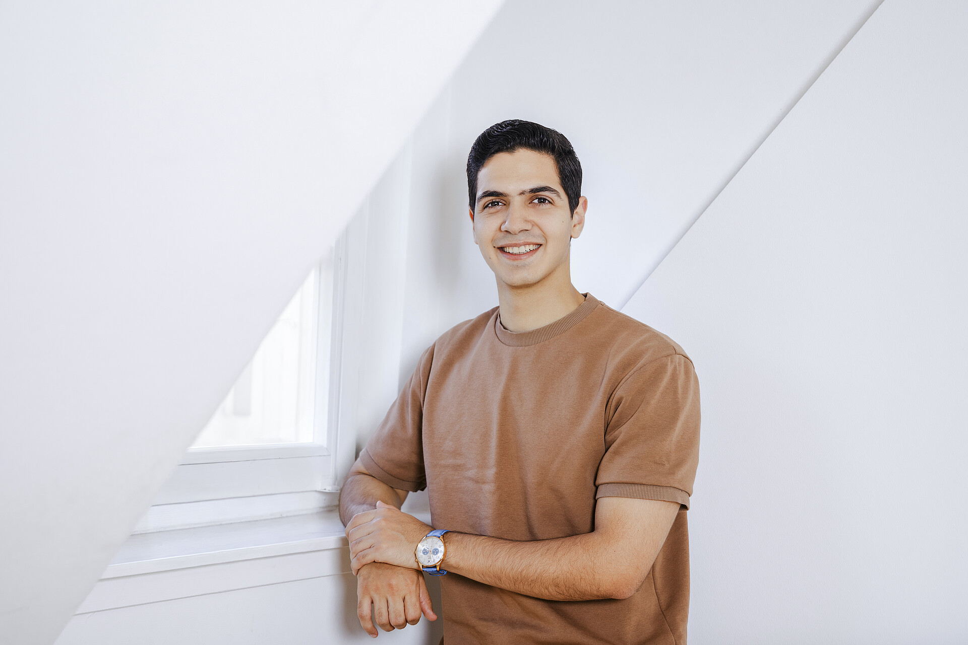Lächelnder Mann im braunen T-Shirt an einer Fensterbank.