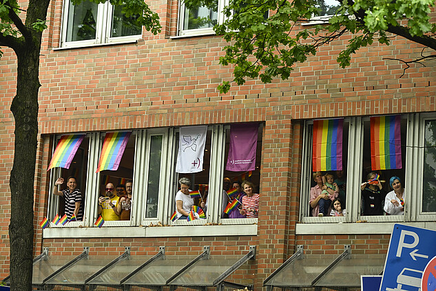 Menschen stehen am Fenster und winken zum CSD