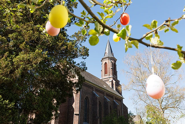 Eine Kirche, davor ein Baum mit Ostereiern