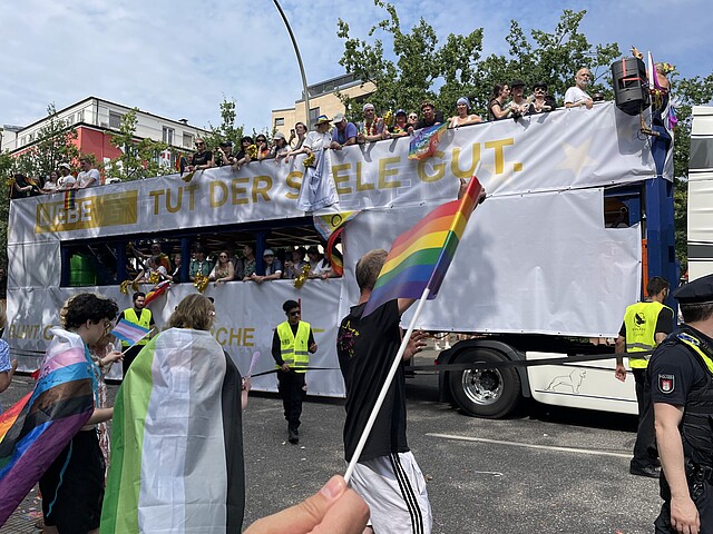 Truck der Evangelischen Kirche Hamburg beim Christopher Street Day 2025 in Hamburg mit dem Banner „Liebe tut der Seele gut“, Menschen mit Regenbogenflaggen feiern vor und auf dem Wagen.