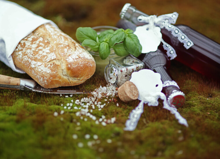 Brot, Salz, Messer, Bailikum und Getränk auf einem mit Moos bewachsenen Stein