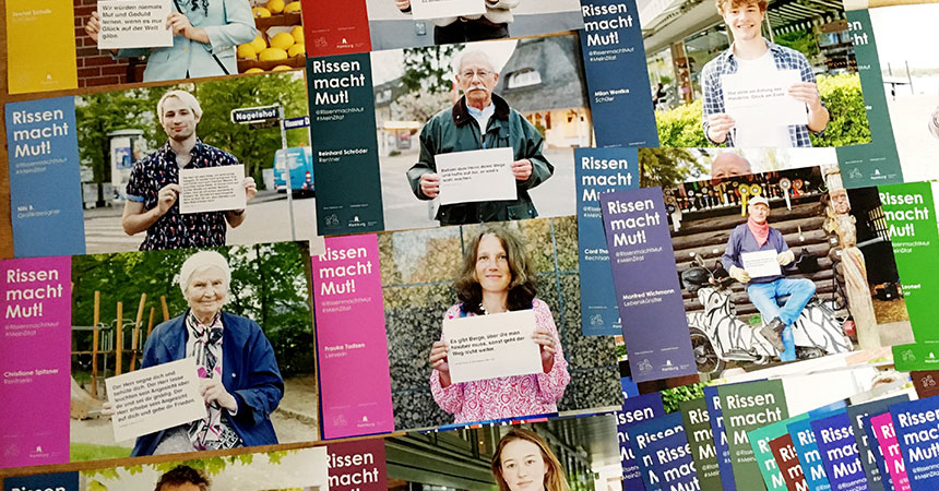 Mehrere Plakate der Aktion "Rissen macht Mut" liegen auf dem Biden aus