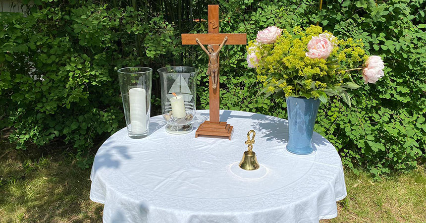 Tisch mit Kreuz, Kerzen und Blumen